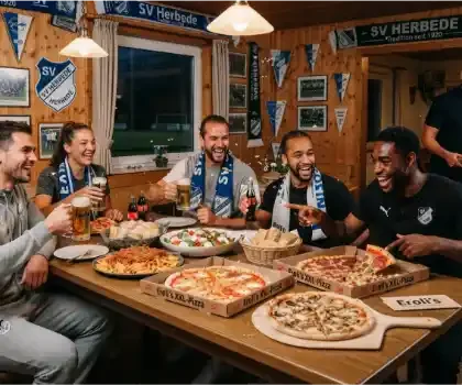 Ein stimmungsvolles Foto, das ein gemütliches Vereinsheim des Fußballvereins SV Herbede zeigt, in dem eine fröhliche Gruppe von Vereinsmitgliedern nach dem Training oder Spiel gemeinsam das Catering von Eroli's genießt. Fünf gut gelaunte Sportlerinnen und Sportler sitzen an einem rustikalen Holztisch, der reich mit blau-weißen Vereinsschals, Gläsern mit Bier und Cola sowie einem großzügigen Catering-Angebot gedeckt ist. Auf dem Tisch stehen zwei große Pizzakartons mit der Aufschrift „Eroli's XXL-Pizza“, eine frische Pizza auf einem Holzbrett, eine große Schale Penne Bolognese, ein Caprese-Salat und frisches Brot im Korb. Im Hintergrund bringt ein freundlicher Eroli's-Zusteller in einem schwarzen Polo-Shirt und mit einer Liefertasche weitere Pizzen. Die Holzvertäfelung an der Wand ist mit historischen Vereinsfotos, Wimpeln und Schals mit der Aufschrift „SV Herbede – Tradition seit 1920“ geschmückt. Die Szene strahlt eine warme, gesellige und kameradschaftliche Atmosphäre aus.